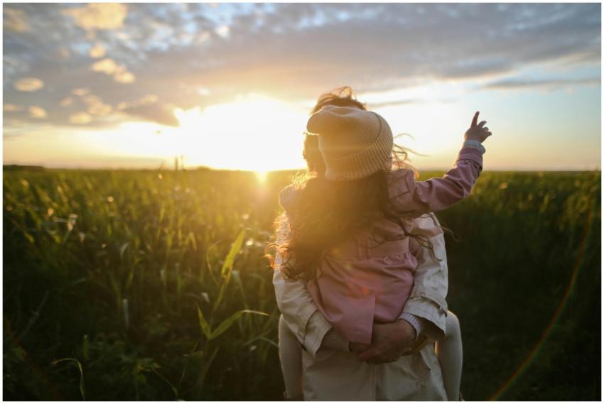 A mother and daughter embrace and point at the sun