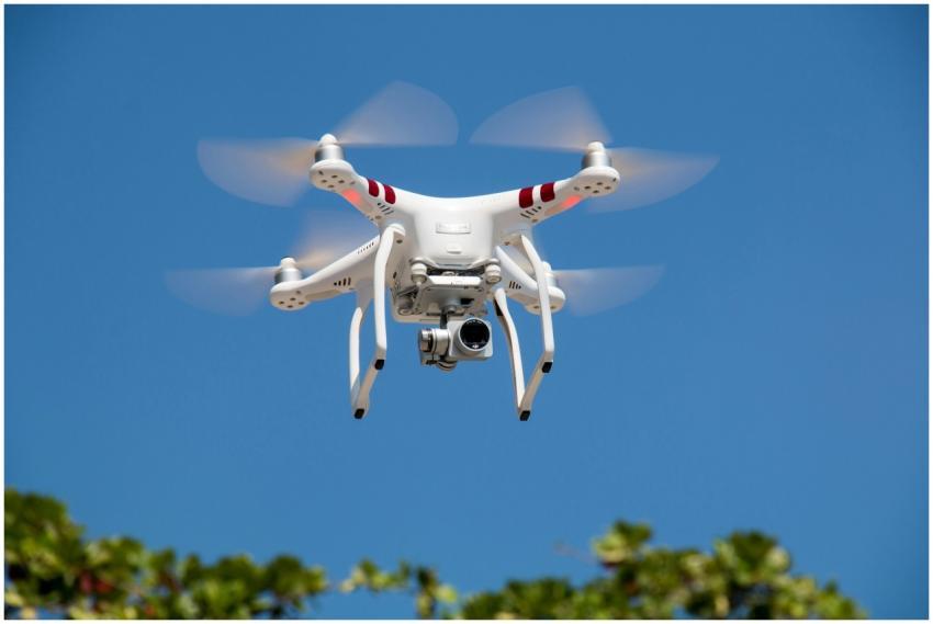A white drone flying with camera against a clear b