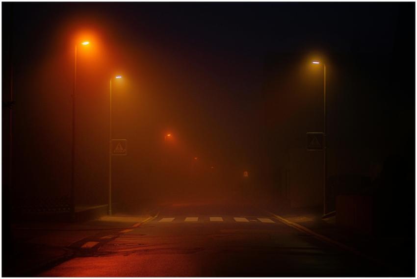 A foggy street scene illuminated by streetlights,