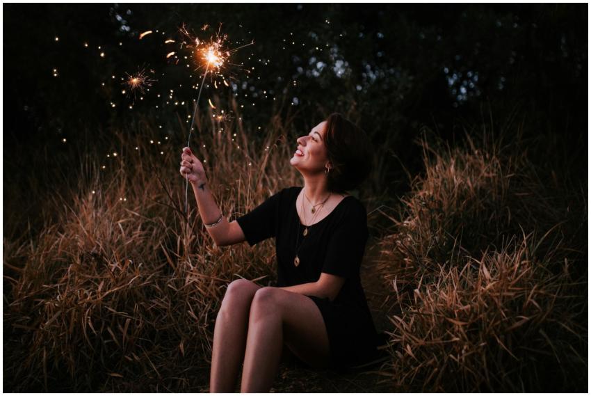 A smiling woman enjoying sparklers outdoors in a g
