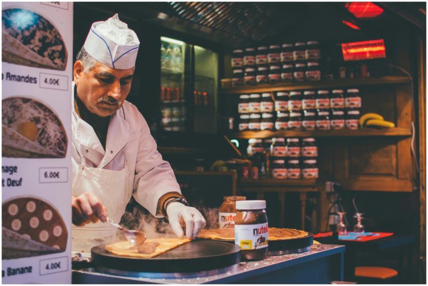 A chef skillfully prepares a Nutella crepe in a co