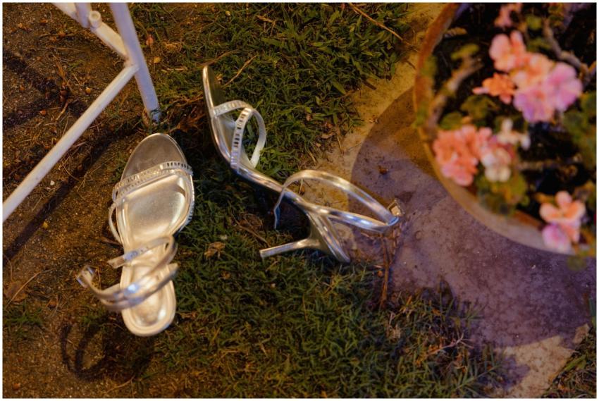 Silver high heel shoes left on grass beside flower