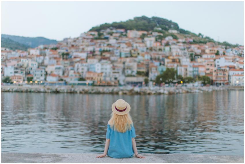A woman in a blue dress sits on a pier, gazing at