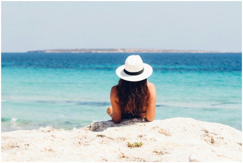 Back view of a woman in a hat relaxing on a rocky