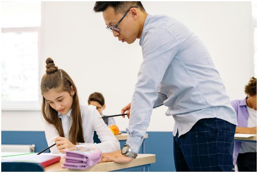 Asian male teacher assisting a young caucasian gir