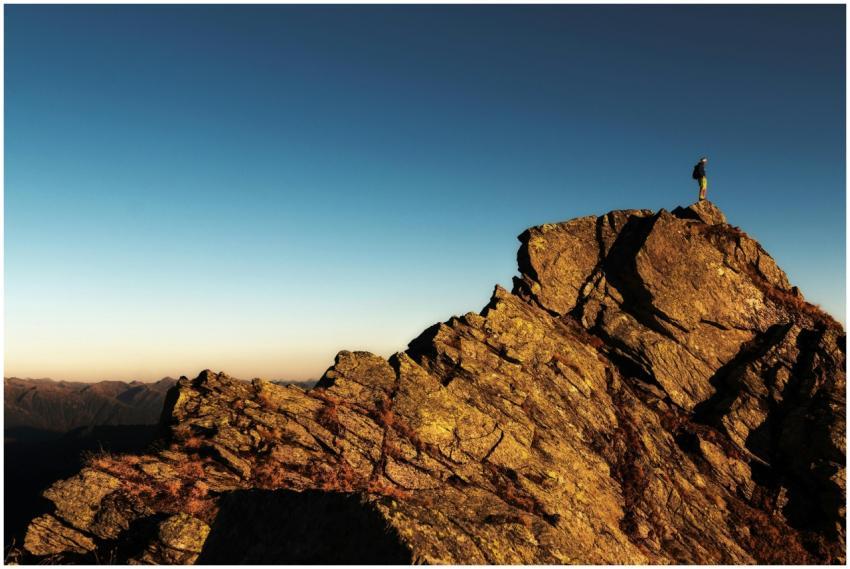 A lone hiker stands triumphantly atop a rocky moun