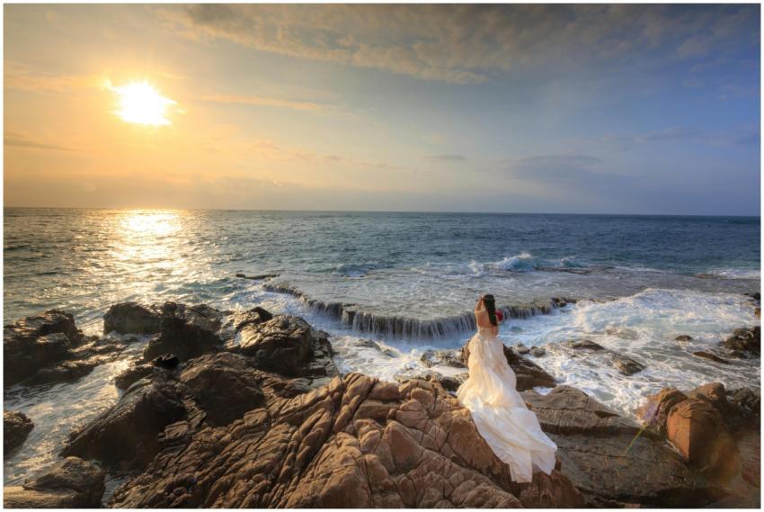 Woman in a white dress standing on rocky shore at