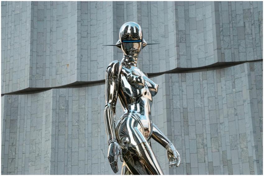 A sleek, chrome humanoid sculpture set before a mi