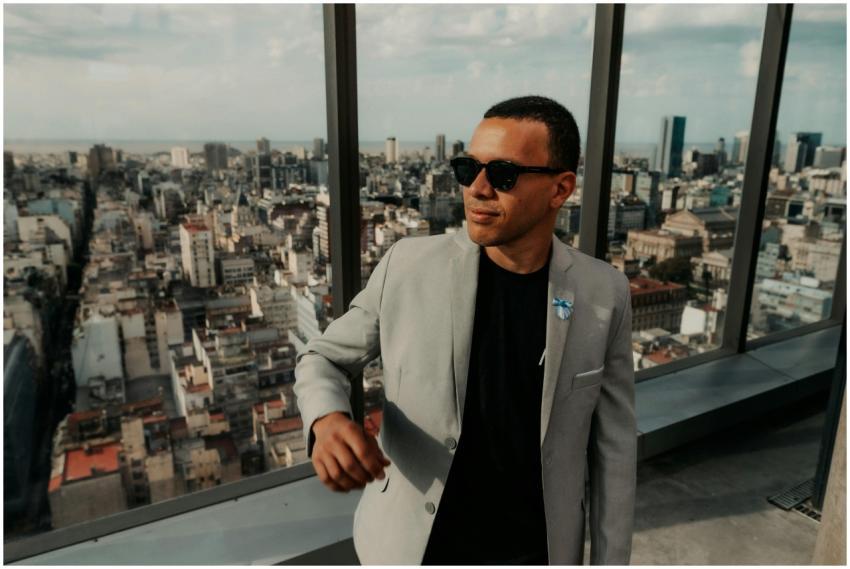 A confident man in sunglasses stands indoors with