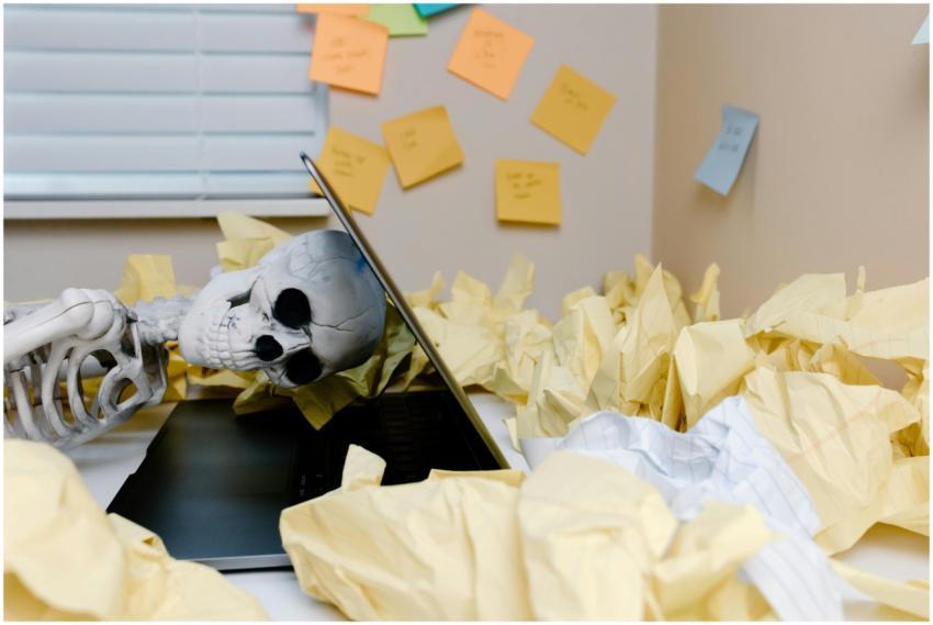 A humorous skeleton slumped over a laptop among cr