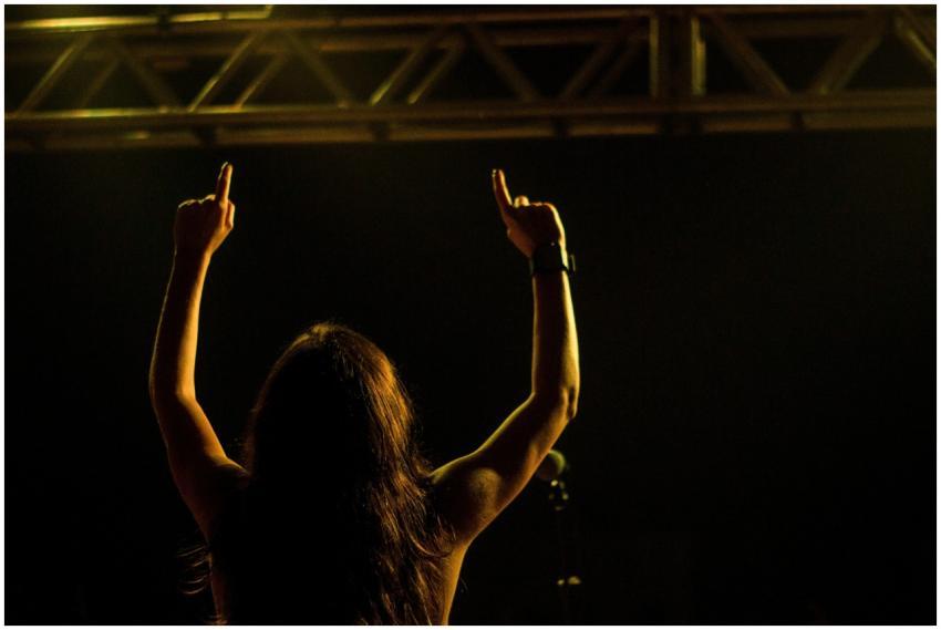 Backlit woman performing on stage, raising arms in
