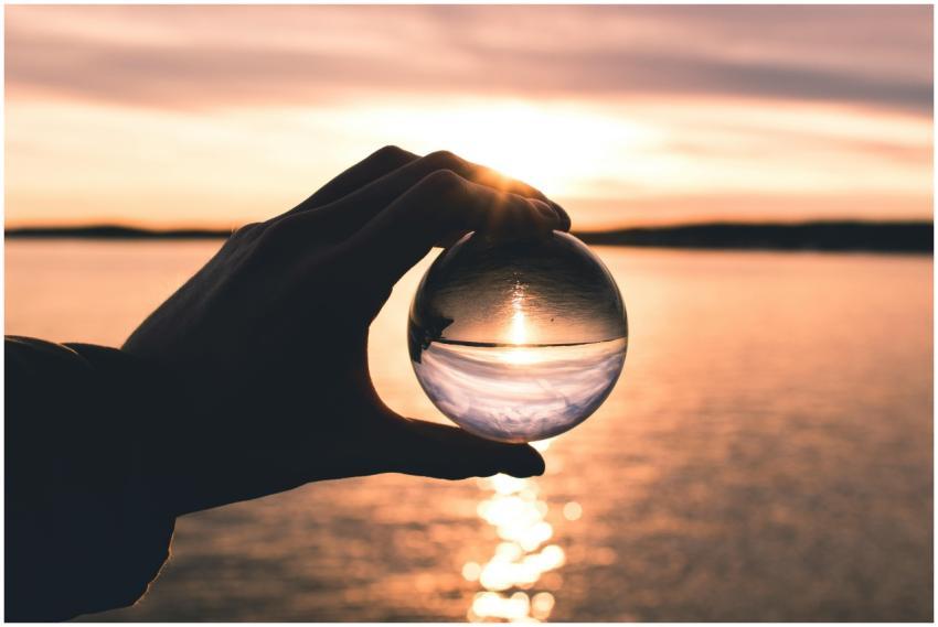 A hand holds a crystal ball reflecting a serene su