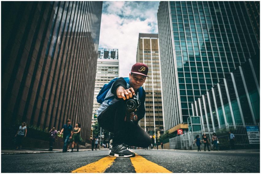 A young man with a camera kneels on a bustling cit
