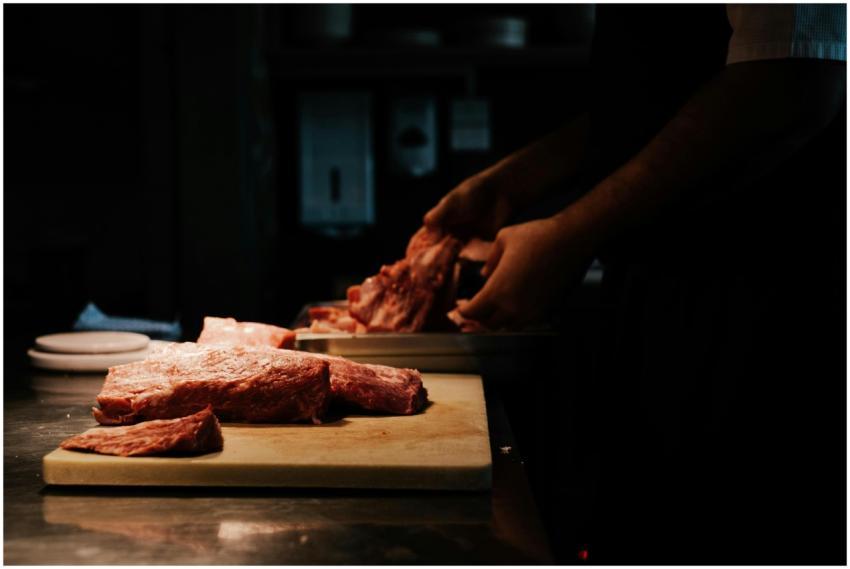 A chef skillfully cuts raw pork on a wooden board