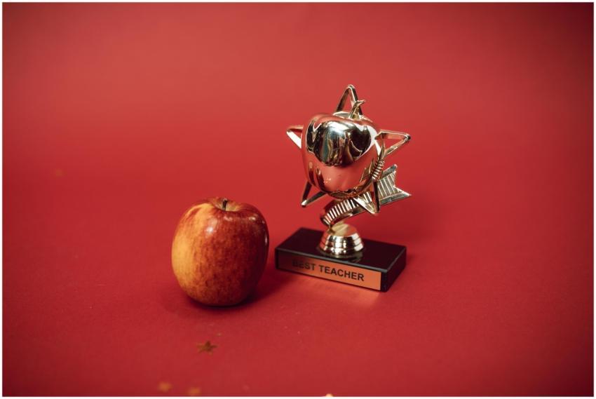 A 'Best Teacher' trophy alongside an apple on a vi