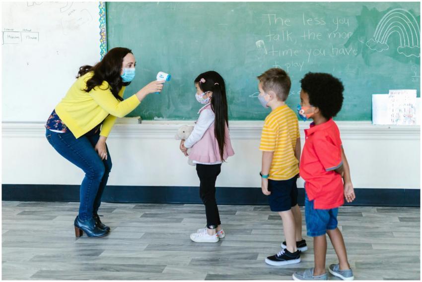 A teacher in a mask checks students' temperatures