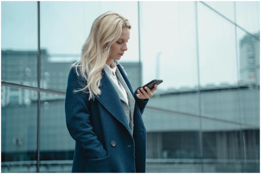 Professional woman in blue coat using smartphone o