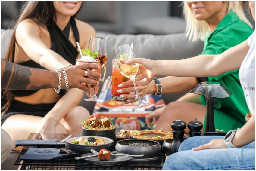 Friends clinking cocktails surrounded by appetizer