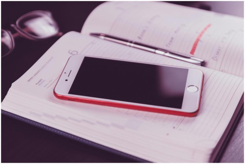 A red and white smartphone on an open diary accomp