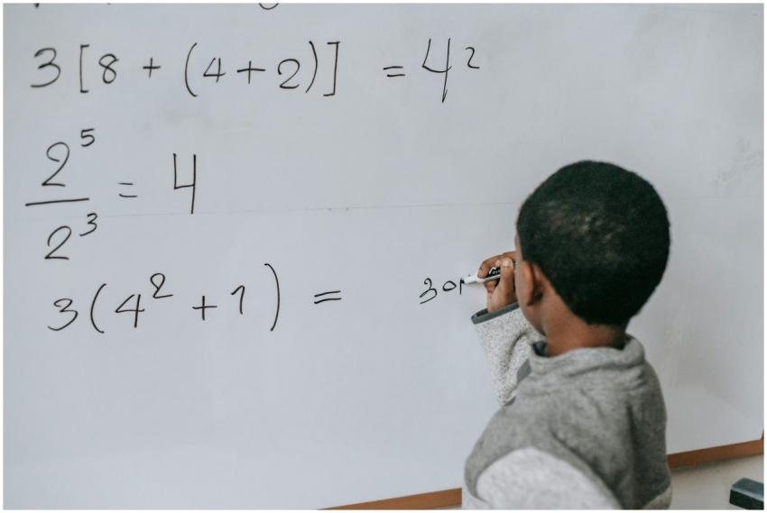 Focused child solving equations on a whiteboard, s