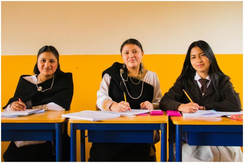 Three students in traditional attire sit at desks,