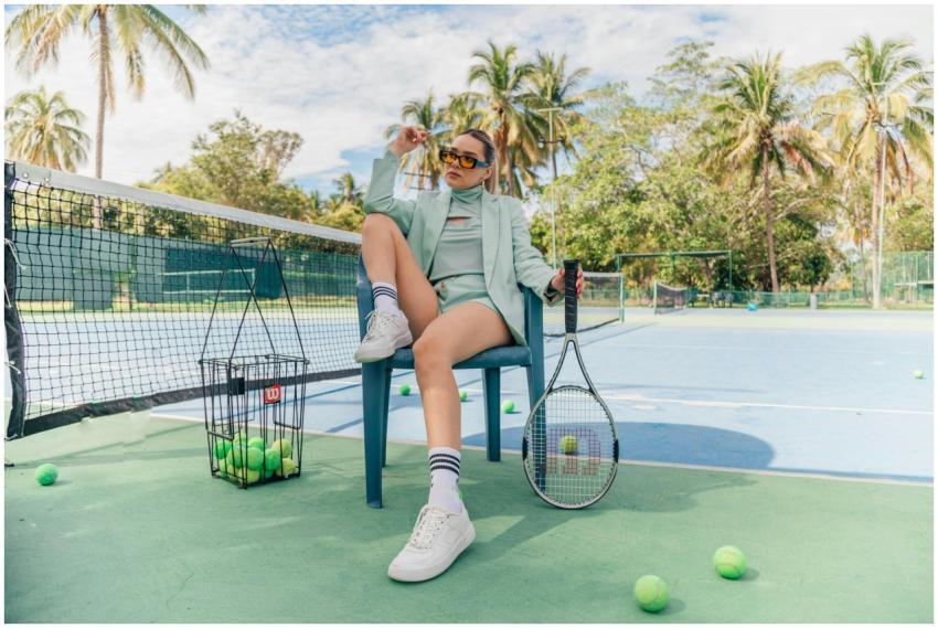 Stylish woman in tennis outfit posing with racket