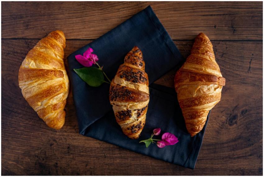 Three croissants with flowers on a rustic wooden t