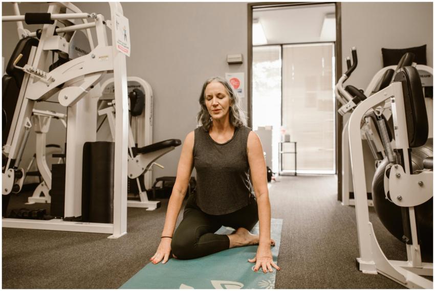 A midlife woman meditates on a yoga mat in a gym,