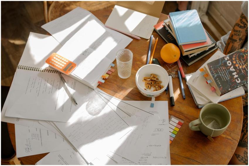 A cluttered study table with books, notes, and stu
