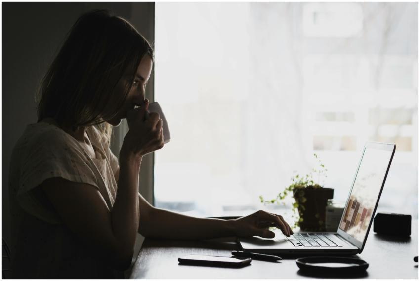 A businesswoman works remotely from home, sipping