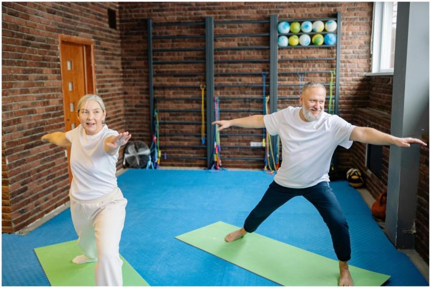 Elderly couple doing yoga poses on mats in a gym,