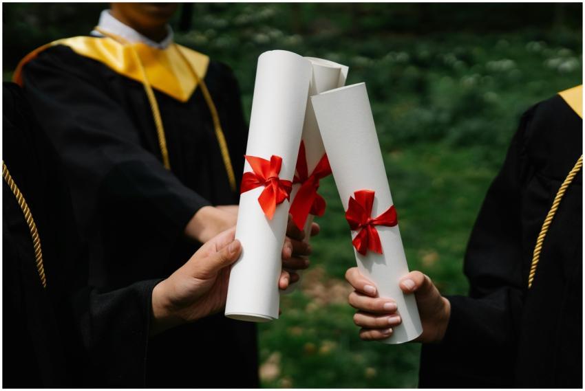 Group of graduates holding diplomas with red ribbo