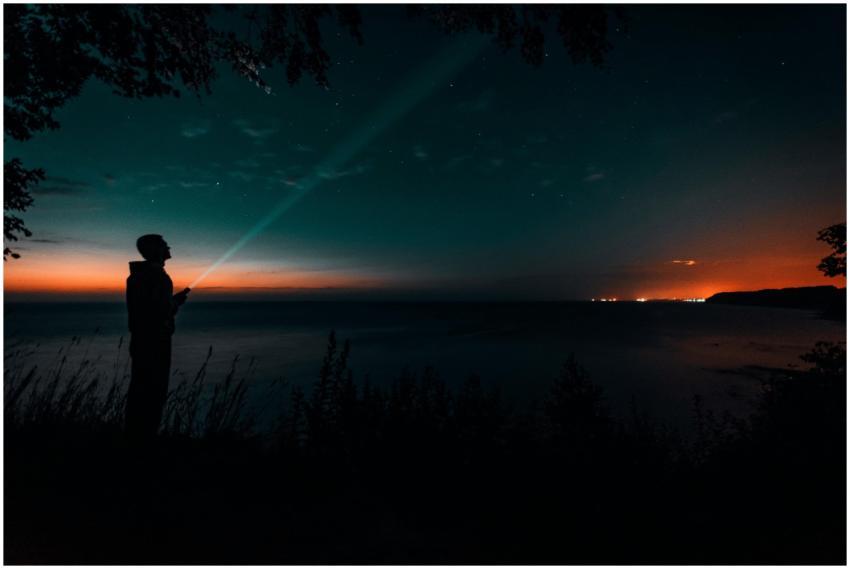 Silhouette of a person with a flashlight by the se