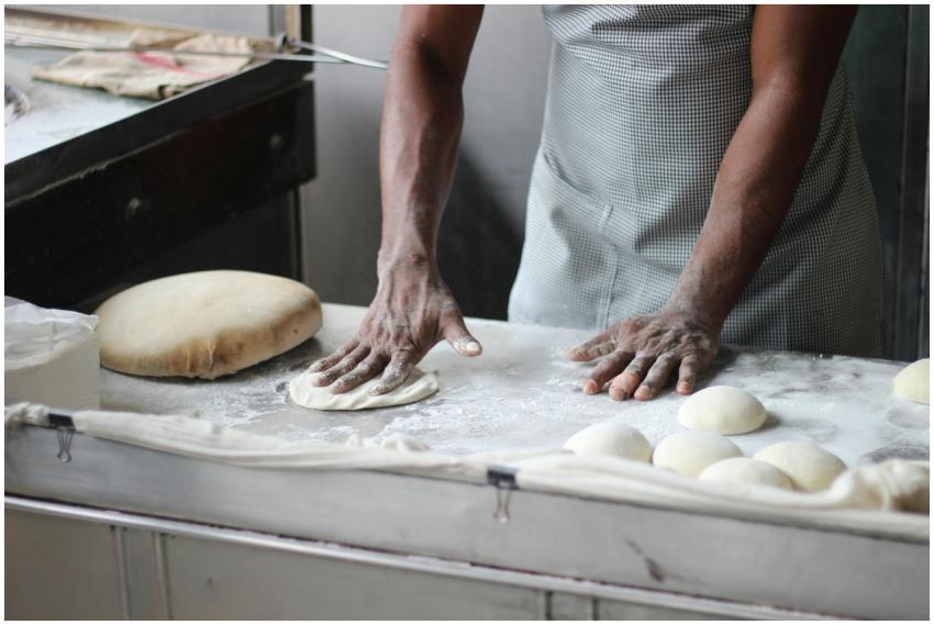 A baker in an indoor kitchen kneading dough for br