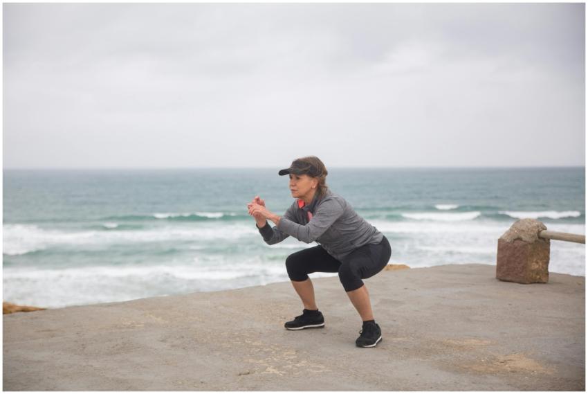 A senior woman performs squats outdoors by the oce