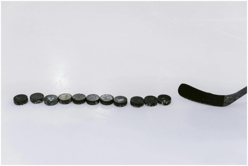 A row of hockey pucks and a stick on an ice rink,
