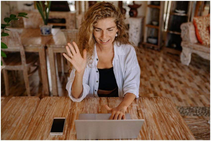 Smiling woman waves during a video call on her lap