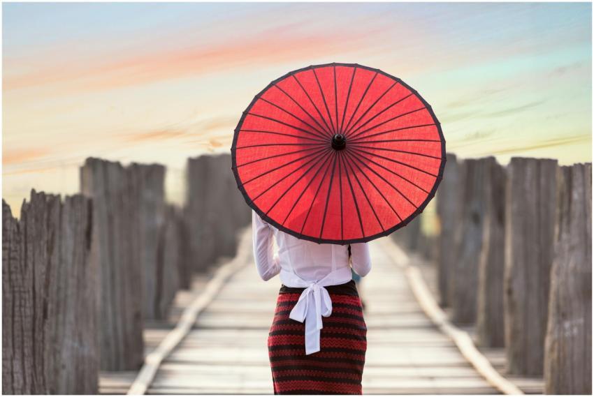 Woman with red umbrella walking on a wooden bridge