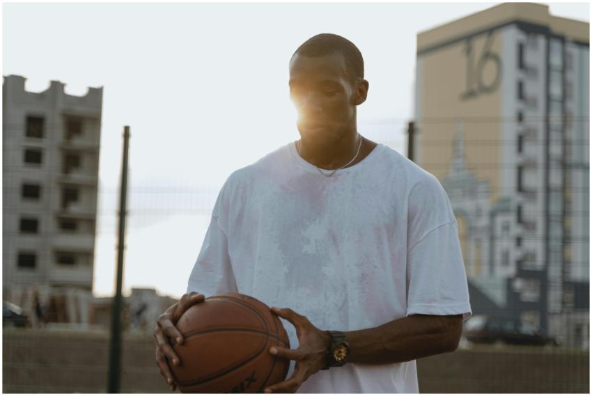 A man holding a basketball outdoors with the sun s