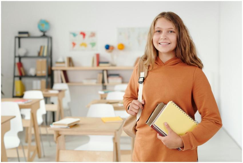 A cheerful schoolgirl in an orange jacket stands i