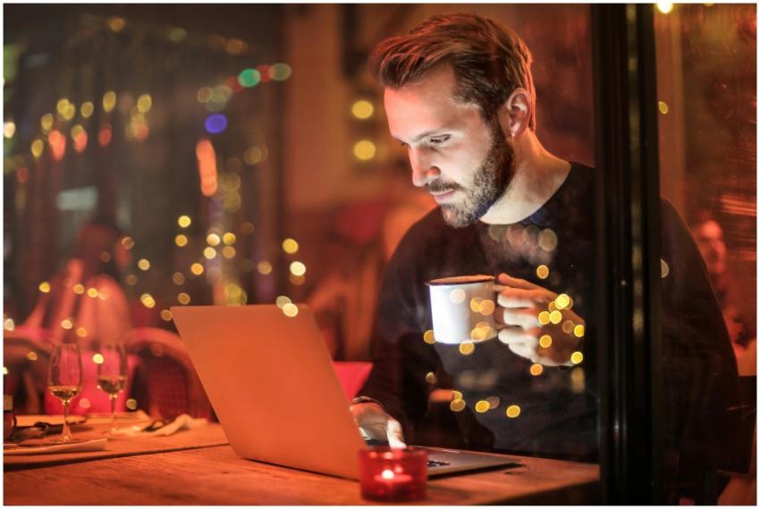 A young man with a beard is working on a laptop at
