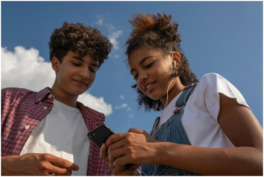 Two teenagers enjoy music together outdoors using
