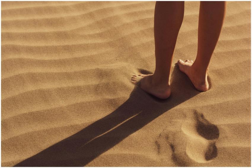 Close-up of a person standing barefoot on sunlit s