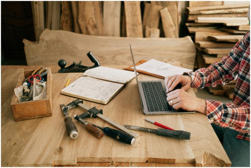 A carpenter using a laptop surrounded by tools in