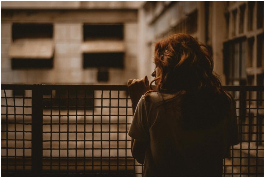 A woman stands alone looking through a railing wit