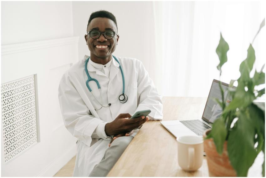 Happy doctor in uniform sitting at a desk using a