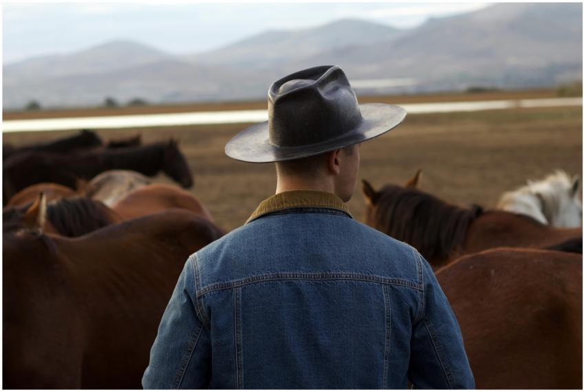 A man in a hat and denim jacket stands amidst a he