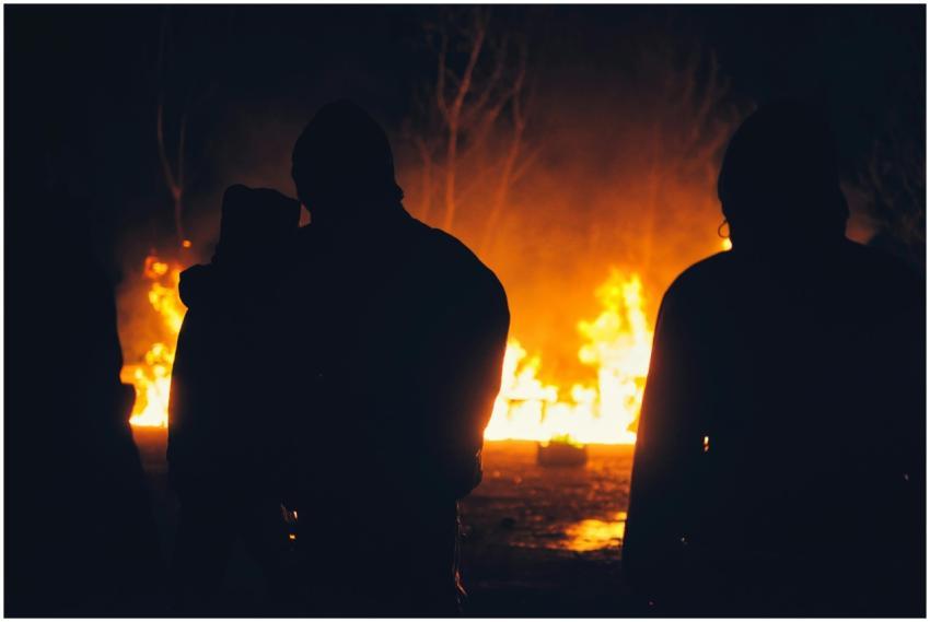 Silhouetted people stand before a blazing fire at