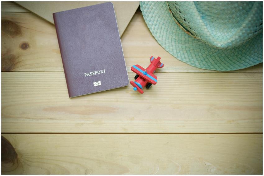 Flat lay of a passport, straw hat, and toy airplan