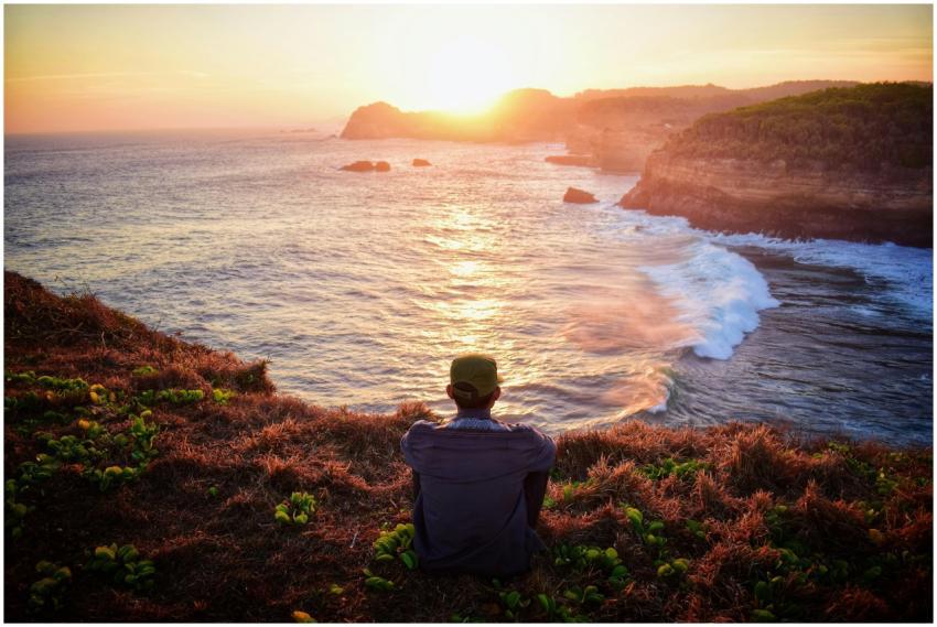 A serene scene of a man sitting on a cliff overloo